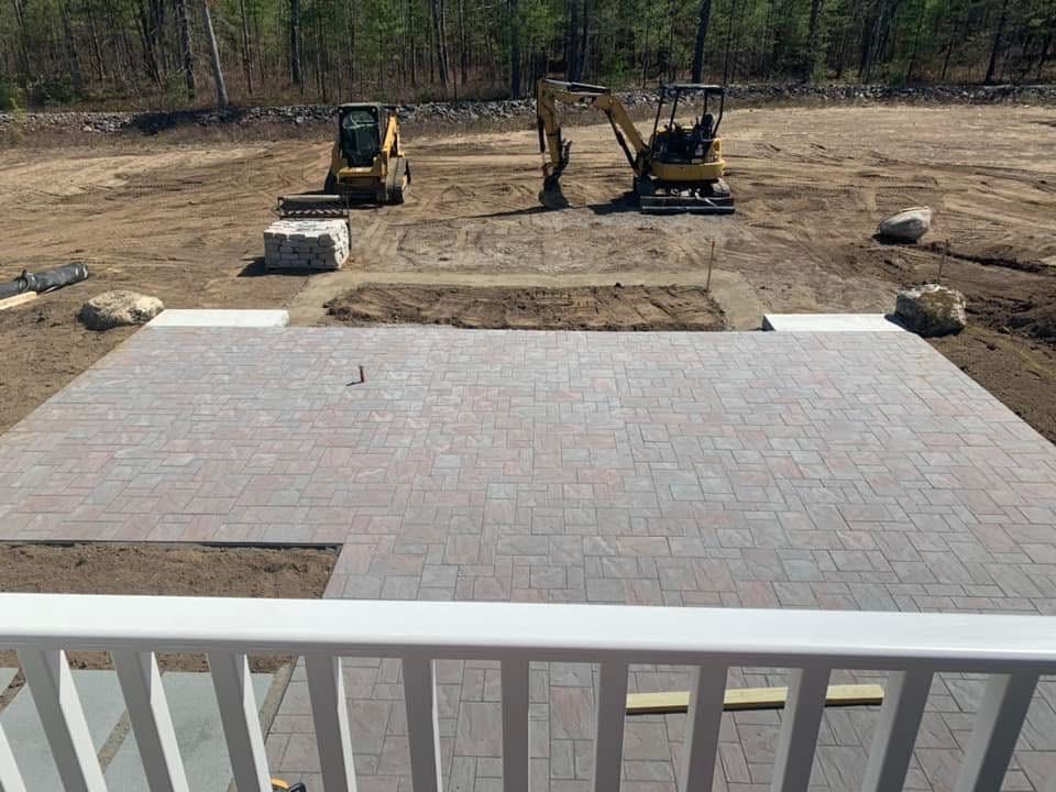 Large stamped paver patio installation with excavation equipment on site
