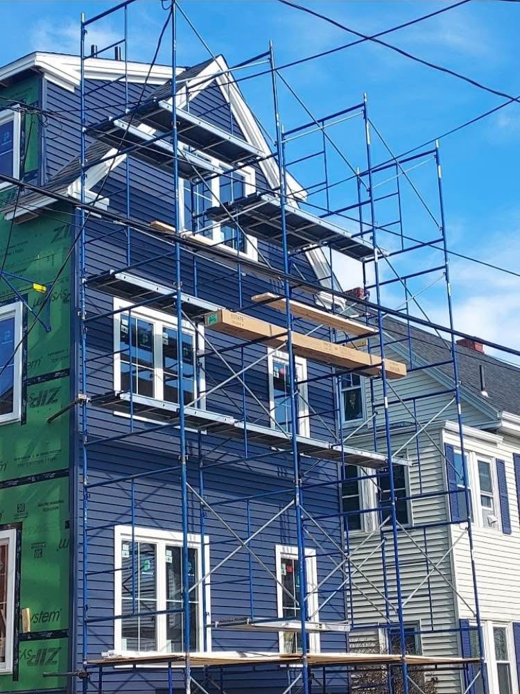Blue siding installation on a three-story home with scaffolding